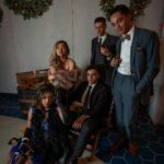 Young adults in vintage attire pose stylishly indoors amid festive wreaths, embodying retro celebration.