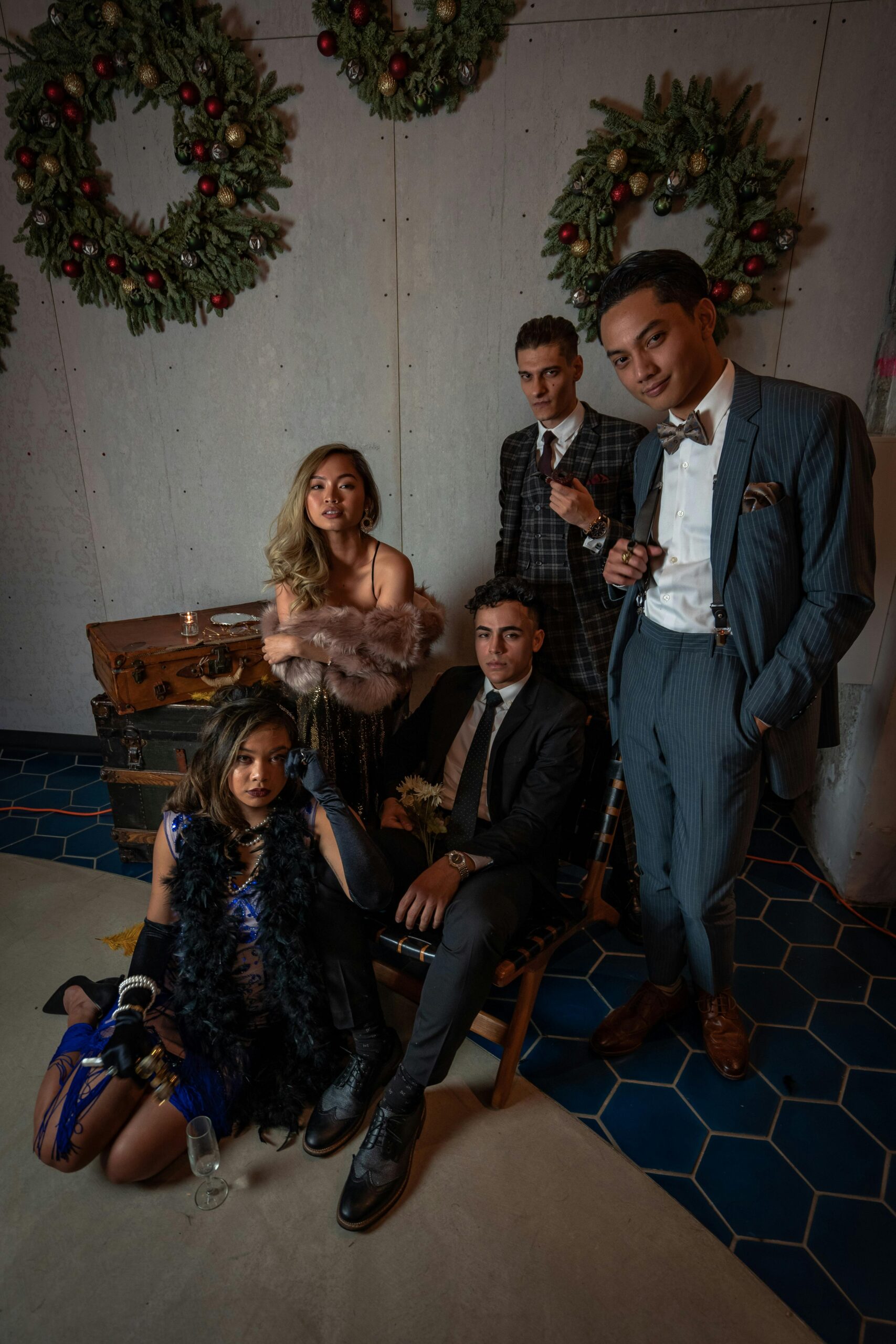 Young adults in vintage attire pose stylishly indoors amid festive wreaths, embodying retro celebration.