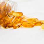 Close-up of fish oil capsules spilling from a bottle on white background.