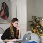 Woman working on a laptop at home, embracing digital nomad lifestyle. Modern workspace with plants.